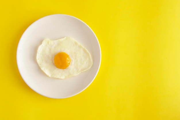 Gebakken eieren op een witte plaat bovenaanzicht minimalistische compositie op een gele achtergrond