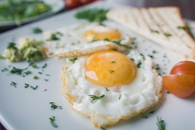 Gebakken eieren op witte plaat met groene en tomaat cherry - ontbijt, macro weergave, close-up