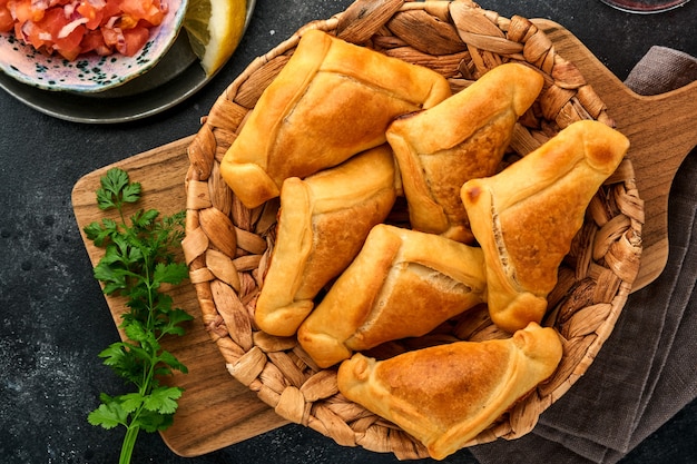 Gebakken empanadas met koriander, vlees, ei, tomaat en chilisaus op zwarte achtergrond. Chileens typisch gerecht. Latijns-Amerikaanse en Chileense onafhankelijkheidsdag concept.