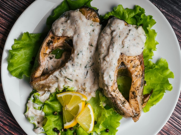 Gebakken forel met roomsaus op witte plaat. Rode vis met citroen en salade