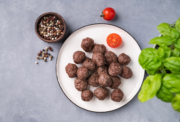 Gebakken gehaktballetjes op een witte plaat op een blauwe achtergrond met verse kruiden, tomaten en specerijen Gehaktballetjes gekookt in de oven Het concept van gezond eten