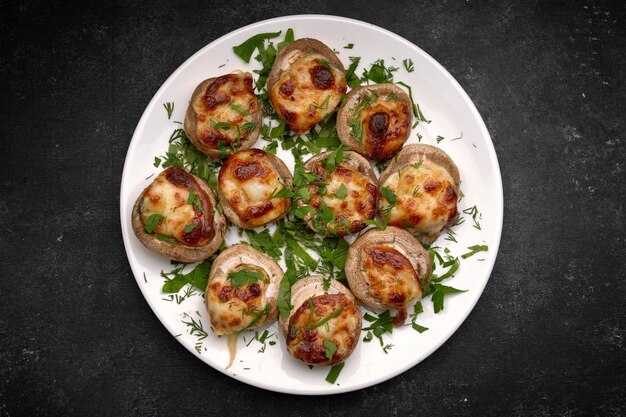 Gebakken gevulde champignons champignons, met kaas en kruiden, op een witte plaat, op een zwarte achtergrond