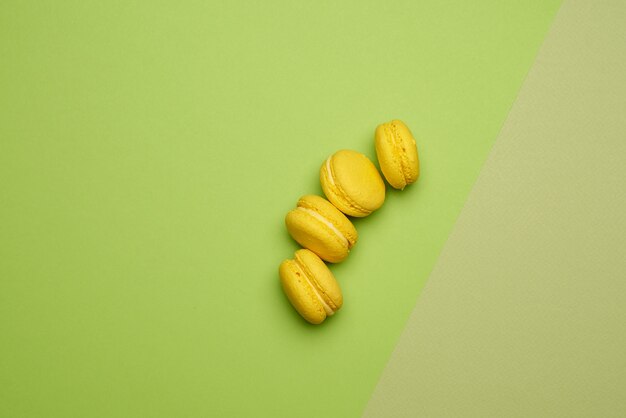 Gebakken groene macaronskoekjes liggen in een rij op een groenbeige achtergrond, bovenaanzicht