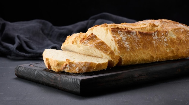 Gebakken heel ovaal brood gemaakt van wit tarwemeel op een zwarte tafel, vers gebak