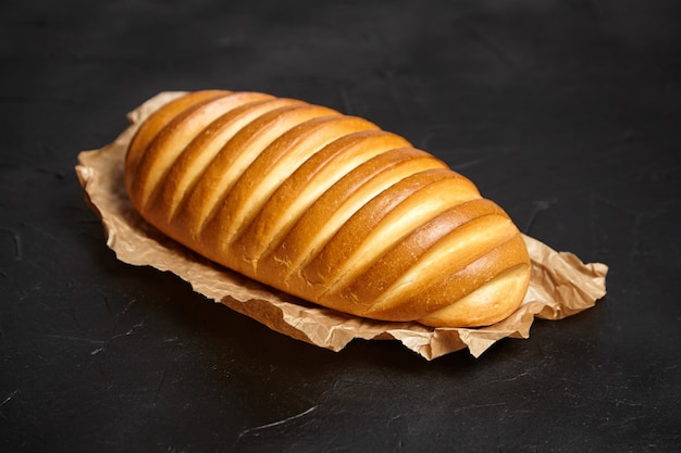 Gebakken hele broodje op donkere stenen tafel. Brood, wit tarwebrood op bakpapier op zwarte achtergrond