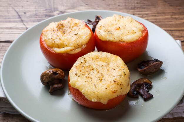 Gebakken hele tomaten gevuld met champignons en kaas met kruiden op een houten tafel. Close-up Selectieve aandacht