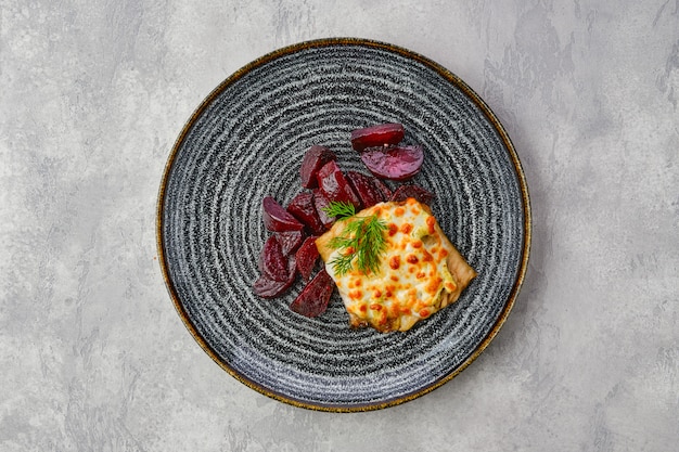 Foto gebakken kabeljauwfilet met gesmolten kaas topping en geroosterde rode biet plakjes op donkere houten tafel