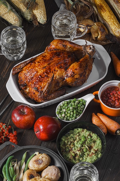 Gebakken kip en gebakken maïs. familie eettafel. gebakken kip en groenten met glazen cider. heerlijk rustiek diner