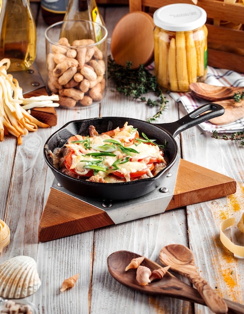 Gebakken kip met tomaten en kaas in gietijzeren pan op de houten versierde tafel