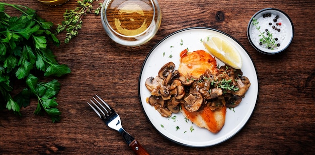 Gebakken kipfilet met champignon champignons en ui in witte wijnsaus met tijm op plaat rustieke houten tafel achtergrond bovenaanzicht