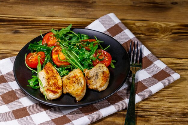 Gebakken kipfilet met salade van verse rucola en kerstomaatjes op houten tafel