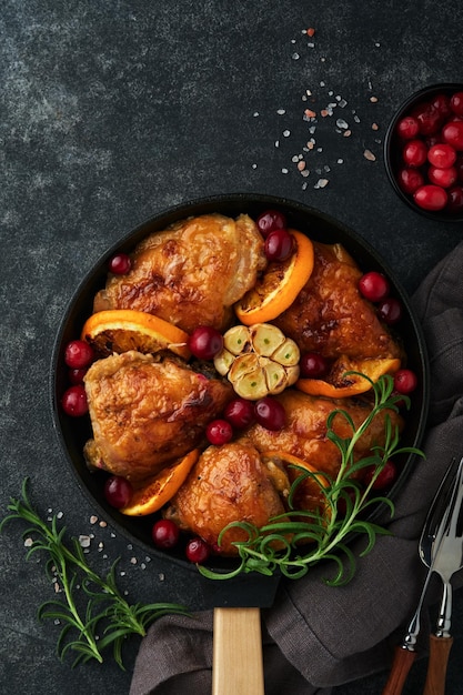 Foto gebakken kippendijen met oranje cranberry en pittige kruiden rozemarijn geserveerd in koekenpan op zwarte betonnen achtergrond feestelijk kerstdiner concept menu bovenaanzicht kopie ruimte