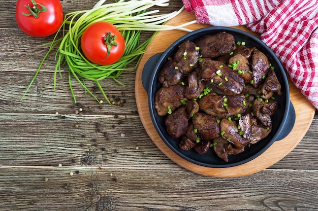 Gebakken kippenlever met jonge groene uien in een gietijzeren koekenpan. lekker gezond gerecht. bovenaanzicht