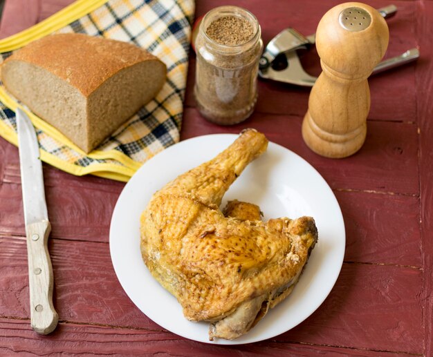 Gebakken kippenpoot op een witte plaat Op een bordeauxrode houten achtergrond Een deel van een zwart brood is in de verte