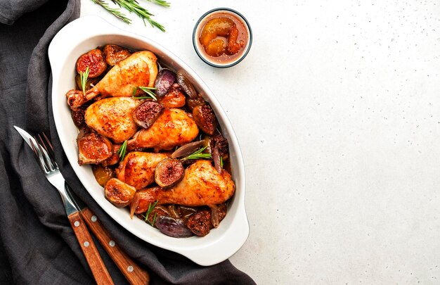 Gebakken kippenpoten drumsticks met vijgen en rode uien in balsamico marinade in keramische ovenschaal witte achtergrond bovenaanzicht