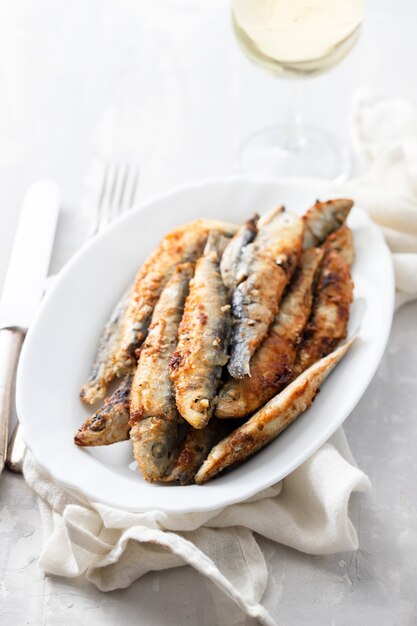 Gebakken kleine sardines op witte schotel op keramische tafel