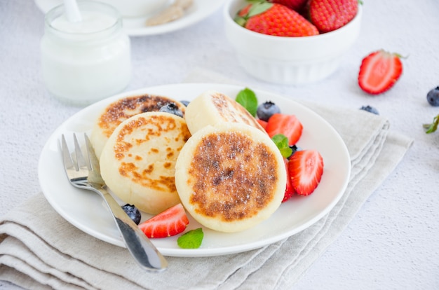 Gebakken kwark pannenkoeken of syrniki met verse bessen op een witte plaat met zure room. Glutenvrij. Traditioneel ontbijt met Oekraïense en Russische gerechten. Horizontaal, close-up