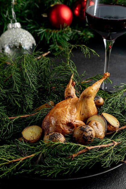 Gebakken kwartel op een bord versierd met groene takken met een glas rode wijn op een donkere kerstachtergrond