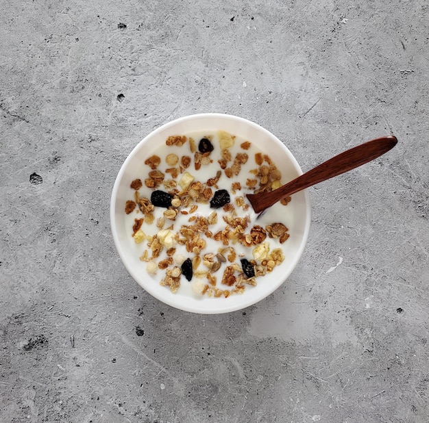 Gebakken muesli met yoghurt, houten lepel in witte kom op lichte achtergrond, bovenaanzicht, plat gelegd.