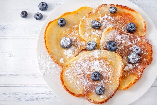 Foto gebakken pannenkoeken met verse bosbessen met poedersuiker op een plaat, close-up, bovenaanzicht