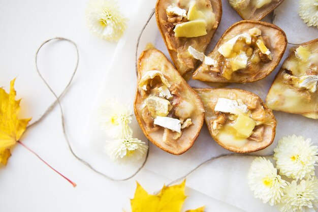 Gebakken peren met brie-kaas en noten tegen de achtergrond van gele herfstbladeren, close-up