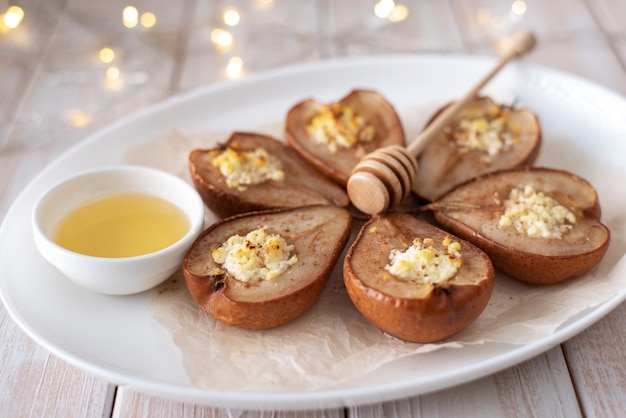 Gebakken peren met kaas, kaneel, honing, op een witte plaat. Kerst dessert.