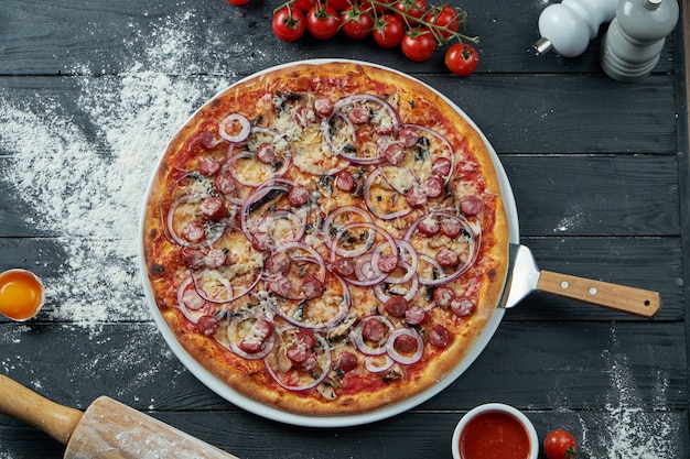 Gebakken pizza met rookworst, rode ui, champignons en gesmolten kaas op een zwarte houten ondergrond in een compositie met ingrediënten. Bovenaanzicht. Italiaanse keuken