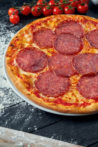 Gebakken pizza met salami chorizo met rode saus en gesmolten kaas op een zwarte houten tafel in een compositie met ingrediënten. Bovenaanzicht