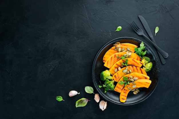 Gebakken pompoen met pompoenpitten en broccoli op een zwarte achtergrond bovenaanzicht vrije ruimte voor uw tekst