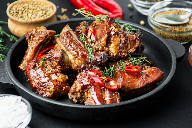 Gebakken ribben in een pan Geroosterde ribben met specerijen en kruiden op een donkere achtergrond Voedselachtergrond Zijaanzicht Close-up