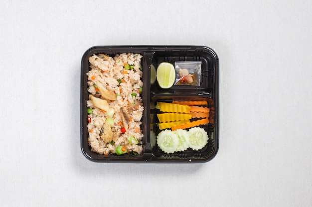 Gebakken rijst met gebakken vis in zwarte plastic doos, op een wit tafelkleed, voedseldoos, Thais eten.