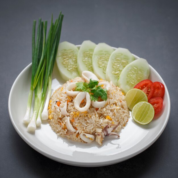 Gebakken rijst met inktvis geserveerd met bosui, komkommer, koriander, tomaat en limoen