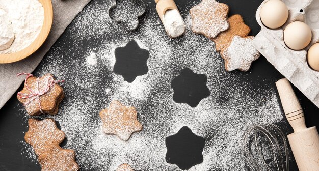 Foto gebakken stervormig peperkoekje met suikerpoeder op een zwarte tafel en ingrediënt