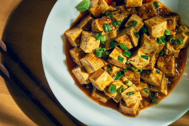 Gebakken tofu in zoetzure saus met Sichuan peper en groenten in een wit bord. Chinese keuken