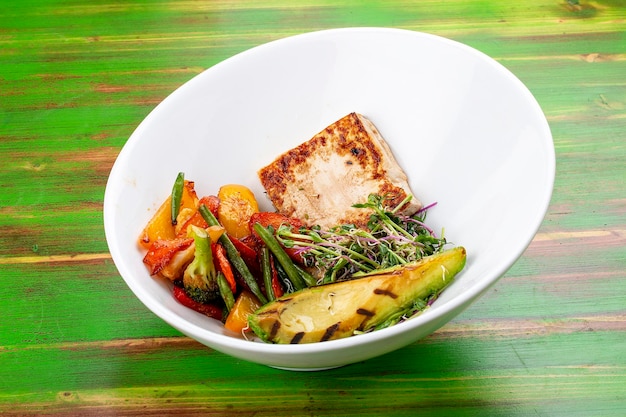 Gebakken tofu met gegrilde avocado en wokgroenten Op een gekleurde houten ondergrond Vegetarische schotel