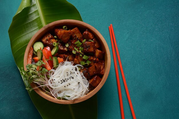 Gebakken tofu met rijstkristalnoedels in een houten kom.