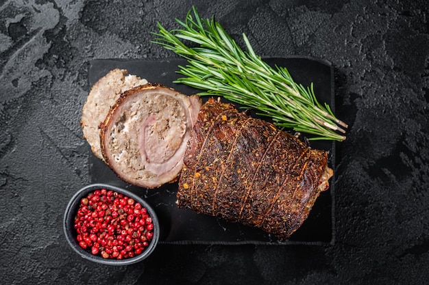 Gebakken varkensrollade Porchetta gerold varkensvlees op een marmeren bord met kruiden Zwarte achtergrond Bovenaanzicht