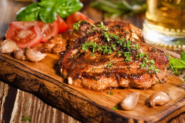 Gebakken varkenssteak op een houten bord om te serveren met groenten en een pul bier.