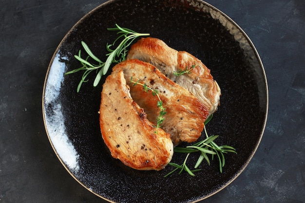 Gebakken varkensvlees steaks op een zwarte plaat op een donkere achtergrond met rozemarijn bovenaanzicht