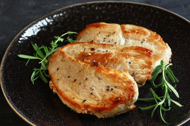 Gebakken varkensvlees steaks op een zwarte plaat op een donkere achtergrond met rozemarijn close-up