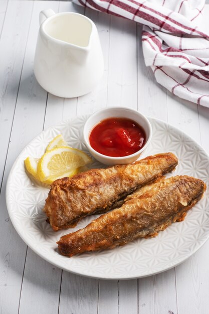 Gebakken vis heek Pollock met tomatensaus en schijfjes verse citroen. Concept eten vette fast food. Witte houten tafel met kopie ruimte.