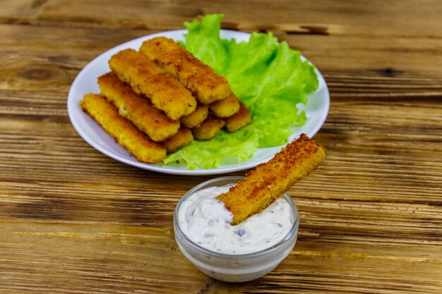 Gebakken vissticks op een bord met sla en tartaarsaus op houten tafel