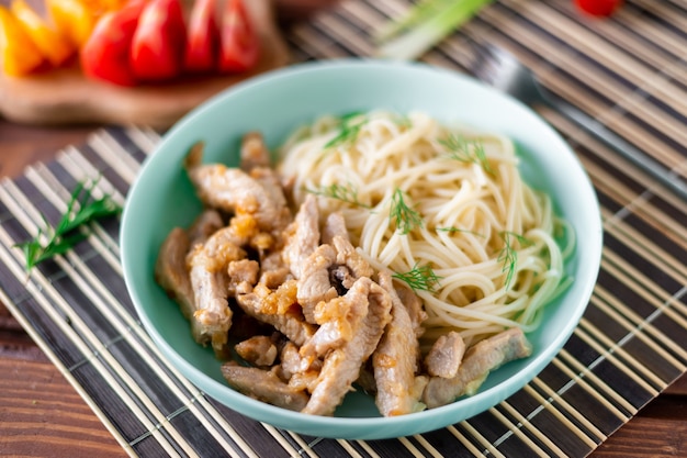 Gebakken vlees en spaghetti op een bord op een houten ondergrond met tomaten en kruiden.