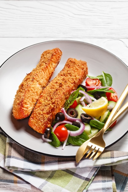 Gebakken zalmfilets gepaneerd met Japanse panko-kruimels geserveerd met groentesalade en citroenwig op een bord op een houten tafel, verticale weergave