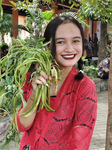 Foto gebaya dorpsmeisje portret van glimlachende jonge vrouw die tegen planten staat