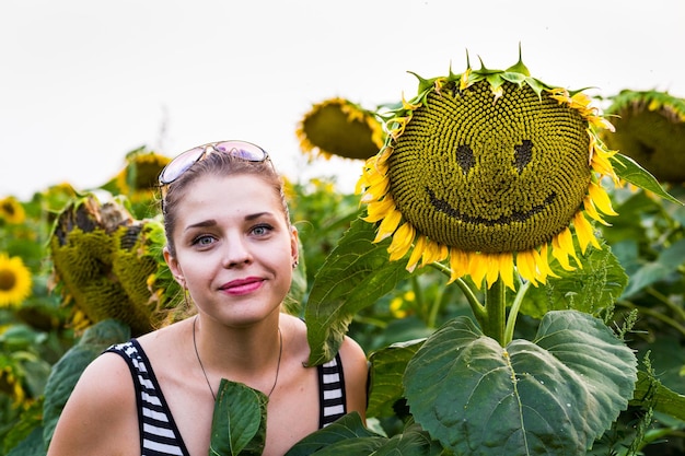 Gebied van bloeiende zonnebloemen en glimlachend mooi meisje op een achtergrondzonsondergang