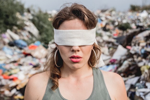 Geblinddoekte vrouwelijke vrijwilliger op een vuilstortplaats van plastic afval. Dag van de aarde en ecologie.