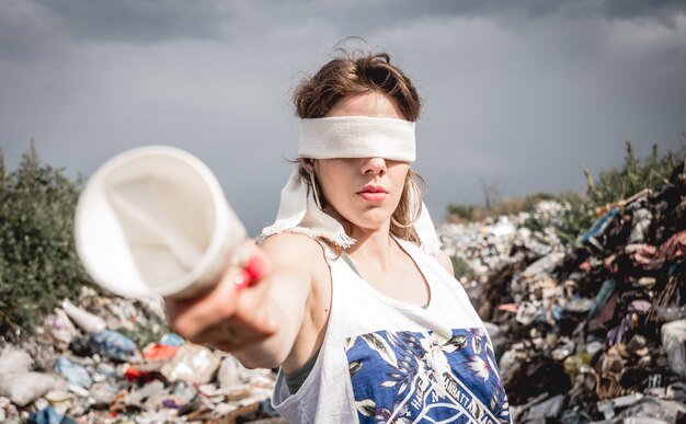 Geblinddoekte vrouwelijke vrijwilliger op een vuilstortplaats van plastic afval.