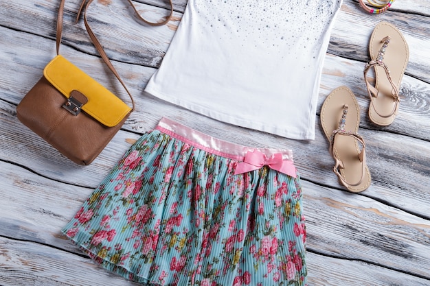 Gebloemde rok en witte top. Top met sandalen en portemonnee. Trendy tweekleurige portemonnee in de uitverkoop. Selectie van zomerkleding voor meisjes.