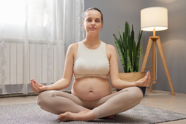 Geboorte wellness routine Welzijn tijdens de zwangerschap Verwachten moeders yoga Rustige ontspannen zwangere vrouw oefenen terwijl ze in de lotuspositie zit mediteren proberen zich te concentreren